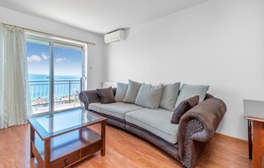 A living room with a sofa, a glass coffee table, and a view of the sea through a balcony. - Apartments Panorama (Crikvenica)