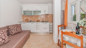 A compact kitchen with white cabinets, a dining table with a lace tablecloth, and a sofa with patterned cushions. - Apartments Neda (Dugi Rat)