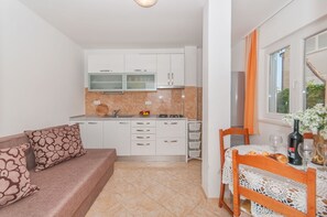 Eine kleine Küche mit weißen Schränken, einem Esstisch mit Spitze und einem Sofa mit gemusterten Kissen.