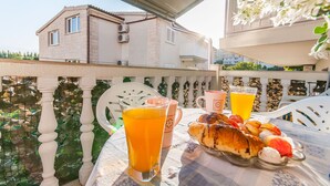 A balcony with a table set for breakfast, including croissants and a glass of orange juice. - Apartments Neda (Dugi Rat)