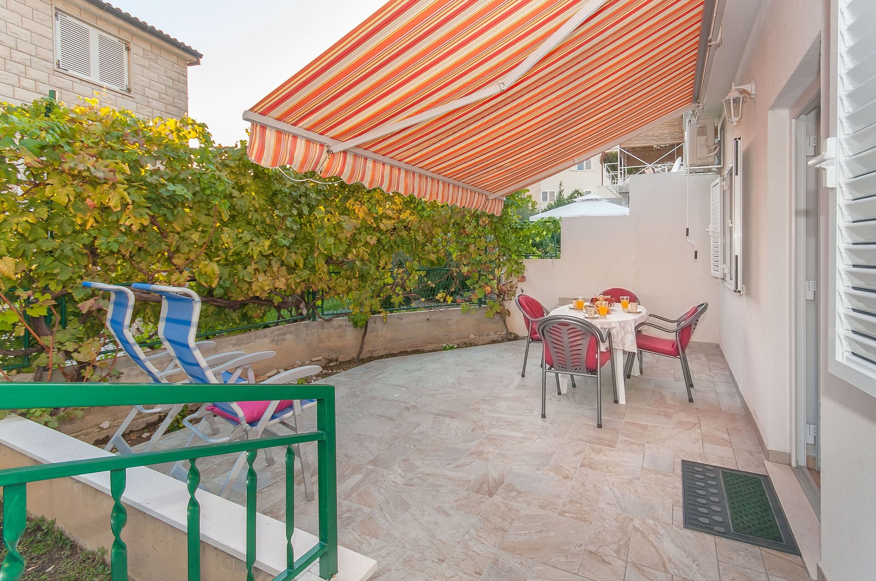 A patio with a striped awning, outdoor seating, and a wall covered in green vines.