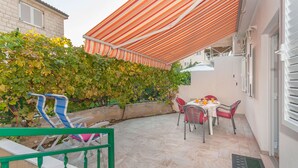 A patio with a striped awning, outdoor seating, and a wall covered in green vines. - Apartments Neda (Dugi Rat)