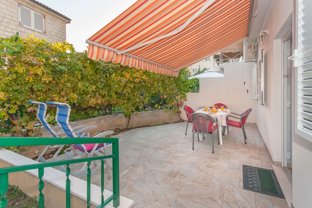 A patio with a striped awning, outdoor seating, and a wall covered in green vines.