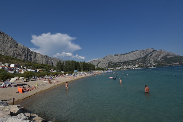 A beach with clear water, rocky mountains in the background, and a few people swimming. - Apartments Neda (Dugi Rat)