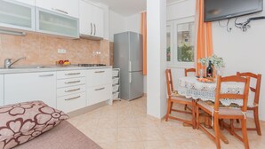 A modern kitchen with white cabinets, a stainless steel refrigerator, and a dining area with a table set for two. - Apartments Neda (Dugi Rat)