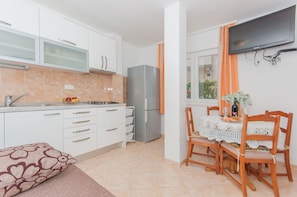 A modern kitchen with white cabinets, a stainless steel refrigerator, and a dining area with a table set for two. - Apartments Neda (Dugi Rat)