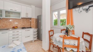 A compact kitchen with white cabinets, a refrigerator, and a dining area with a table set for two. - Apartments Neda (Dugi Rat)