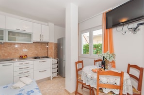 A compact kitchen with white cabinets, a refrigerator, and a dining area with a table set for two. - Apartments Neda (Dugi Rat)
