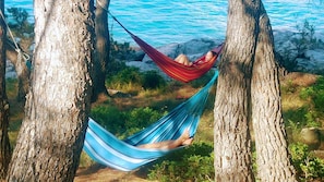 A hammock between two trees by a rocky shoreline with clear blue water. - House Beachouse Natural Park (Selca)