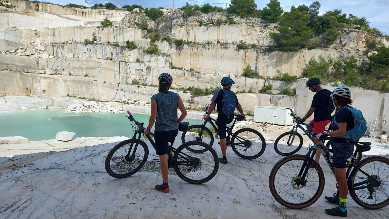 Un groupe de personnes à vélo, près d’une falaise rocheuse et d’une étendue d’eau.