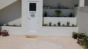 Een witte deur met een bordje voor toiletfaciliteiten, een kleine kamerplant en een stenen sculptuur op een plank.