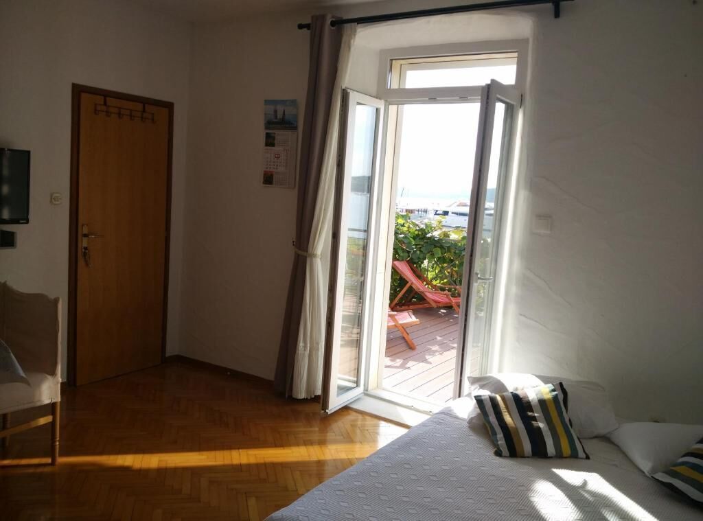 Una stanza con un letto, una porta in legno e una porta scorrevole in vetro che dà su uno spazio esterno con un'amaca e piante.