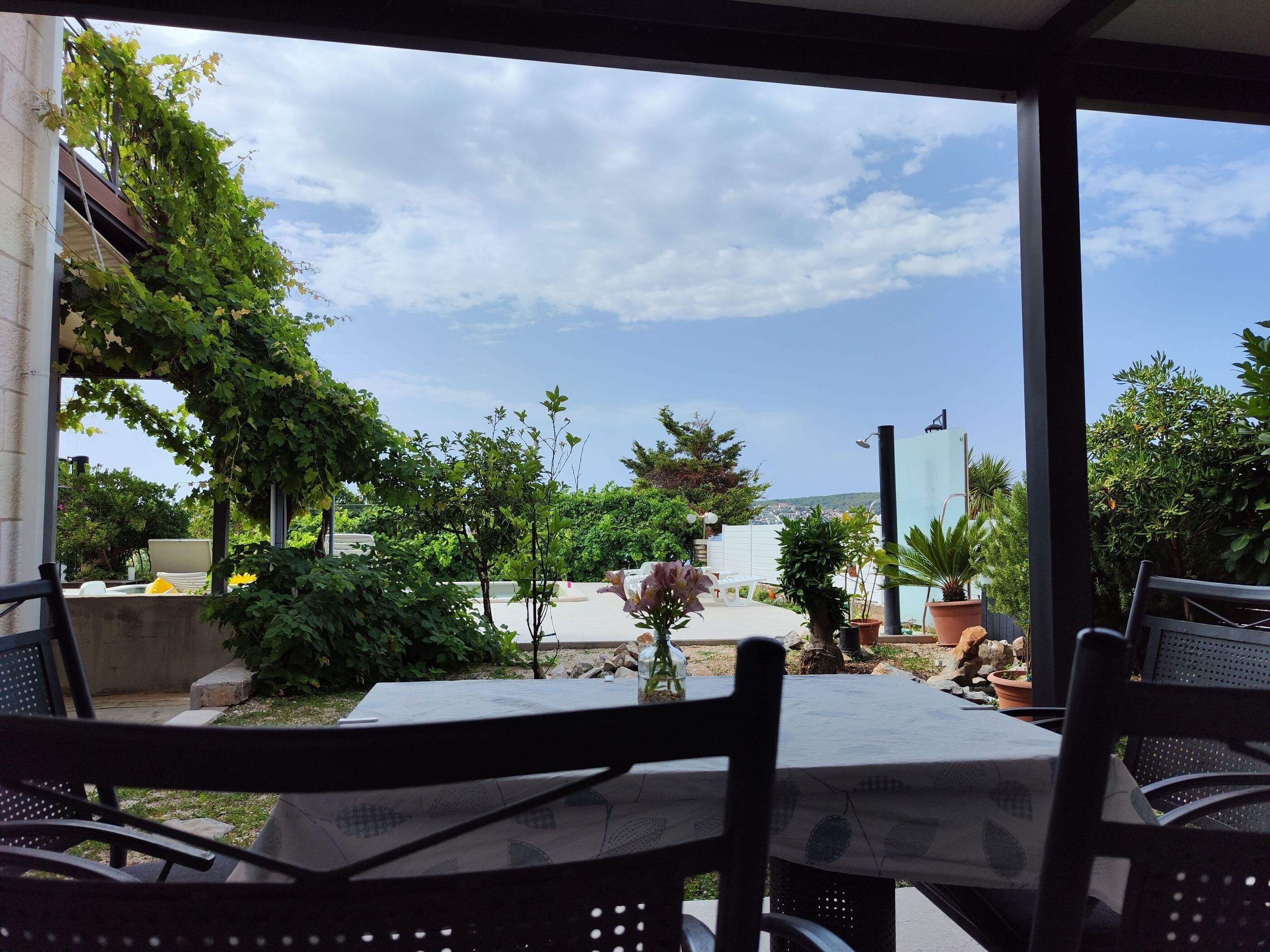 Un patio exterior con una mesa y sillas, rodeado de vegetación y vistas al mar.