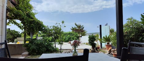 Un patio exterior con una mesa y sillas, rodeado de vegetación y vistas al mar.