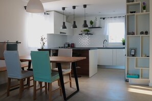 A modern kitchen with white cabinets, a wooden dining table, and pendant lights. - Apartments Ginna (Seget)