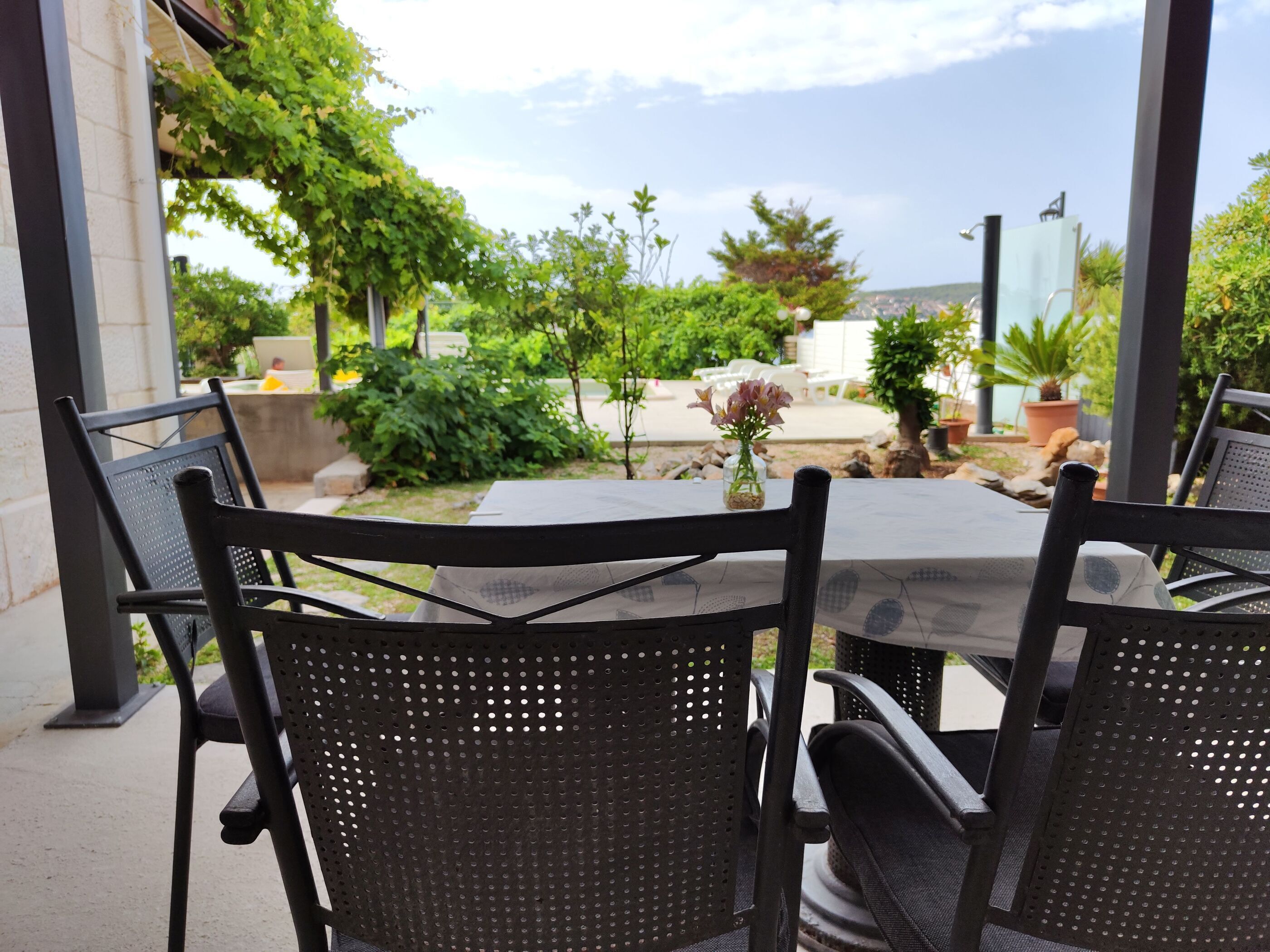 Eine Terrasse im Freien mit Tisch und Stühlen, umgeben von Grünpflanzen und Blick auf die Stadt.