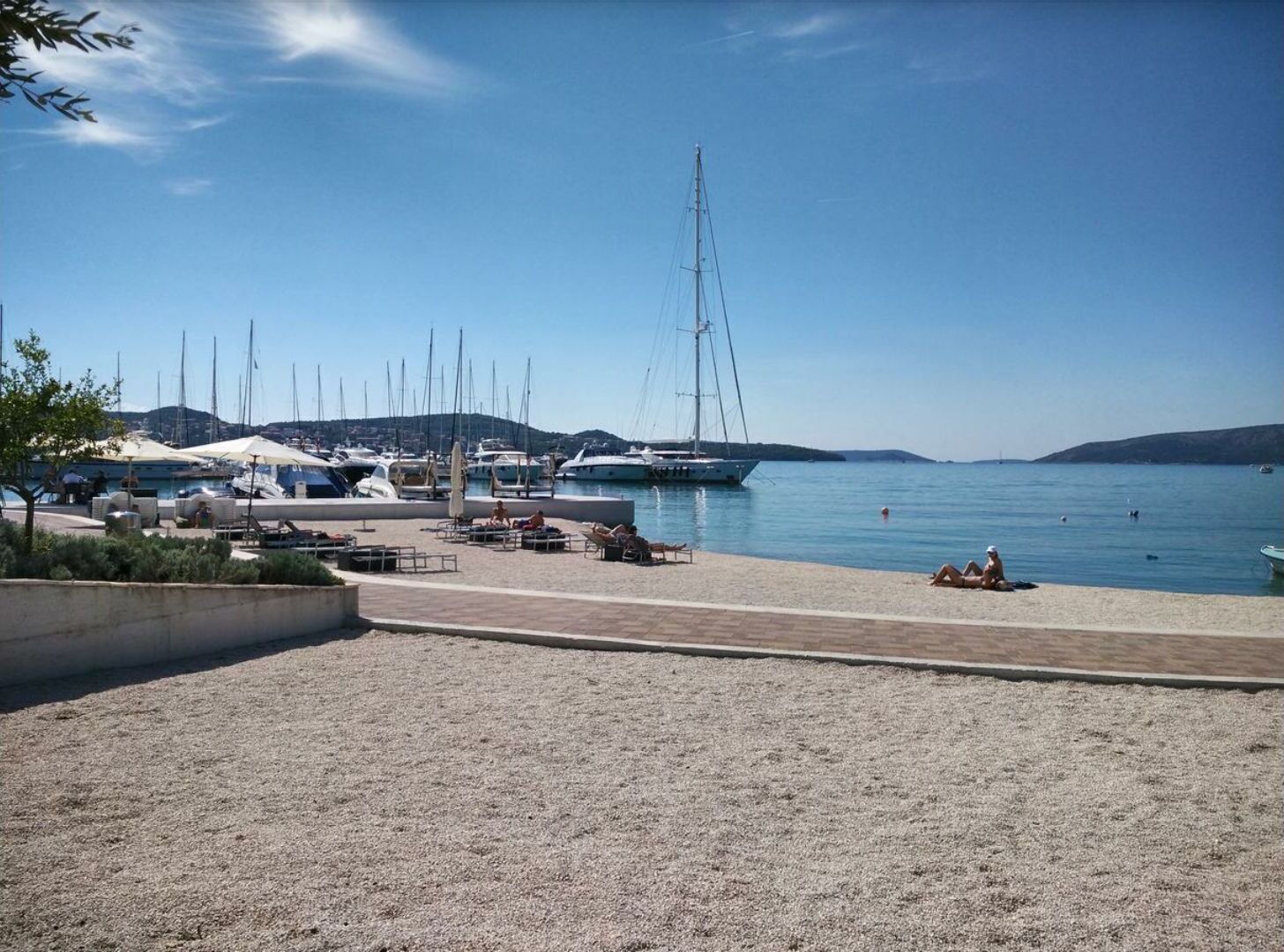 A marina with boats docked, a sandy beach, and a clear sky.