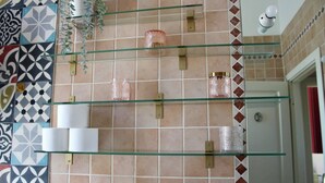 Een badkamer met een betegelde muur, glazen planken en een handdoekrek.