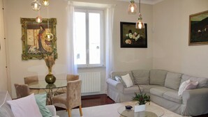 Een woonkamer met een bank, fauteuils, een glazen salontafel, een eettafel met stoelen, en kunstwerken aan de wanden.