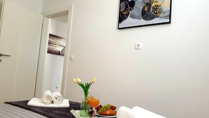 A hotel room with a bed, a painting, a vase with flowers, a fruit plate, and towels. - Apartment Tea (Vodice)