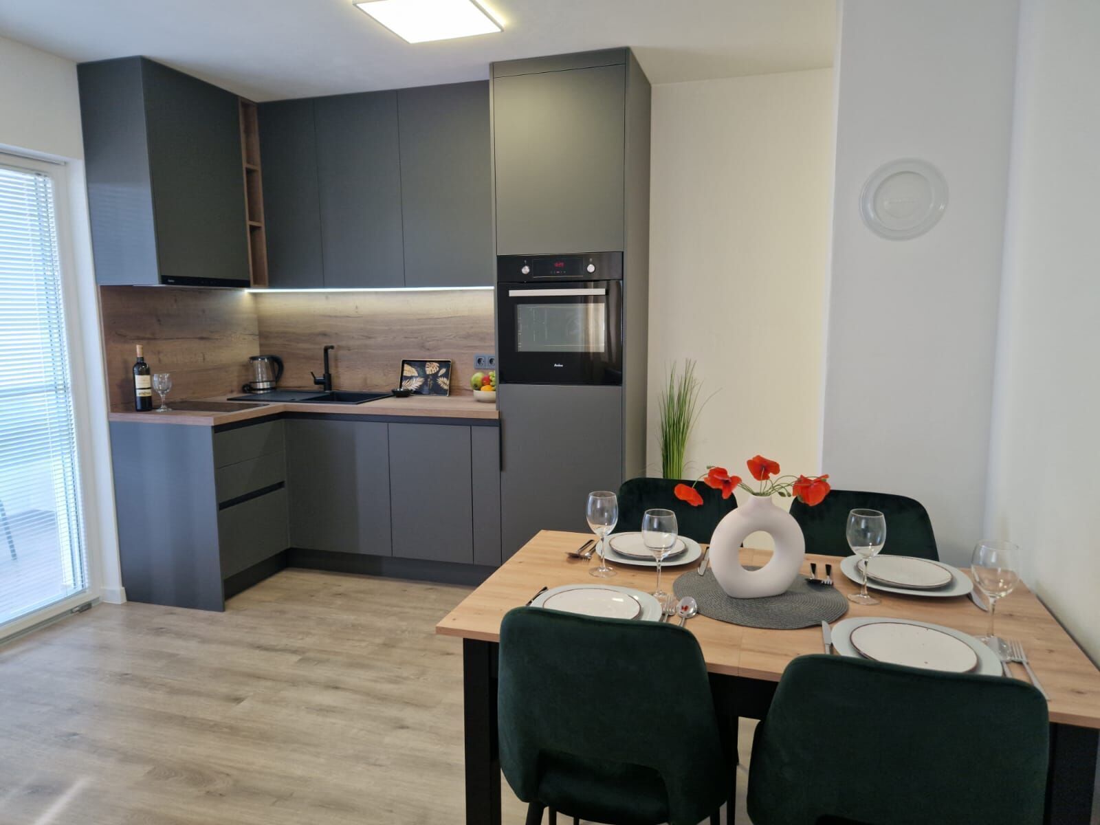 Eine moderne Küche mit dunklen Schränken, einem eingebauten Backofen und einer Essecke mit Tisch für zwei Personen.