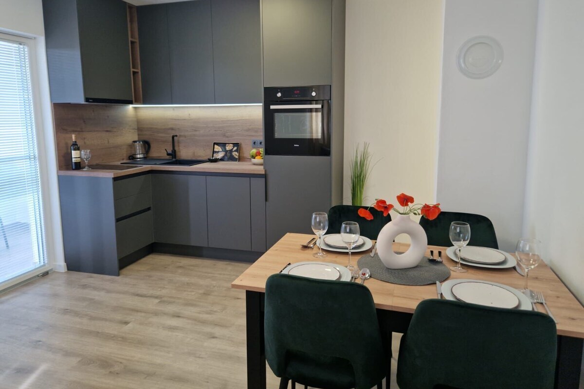 A modern kitchen with dark cabinets, a built-in oven, and a dining area with a table set for two.
