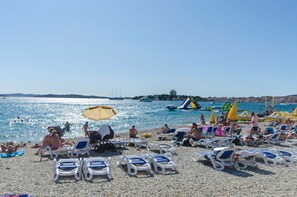 A beach with sun loungers and umbrellas, a water slide, and people swimming. - Apartment Tea (Vodice)