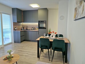 Eine moderne Küche mit grauen Schränken, einem eingebauten Backofen und einem Essbereich mit Holztisch und grünen Stühlen.