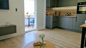 A modern kitchen with dark cabinets, a built-in oven, and a dining area with a round table and chairs. - Apartment Tea (Vodice)