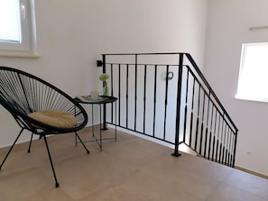 Ein Zimmer mit einem schwarzen Stuhl, einem kleinen Tisch mit einer Vase und einem schwarzen Metallgeländer.