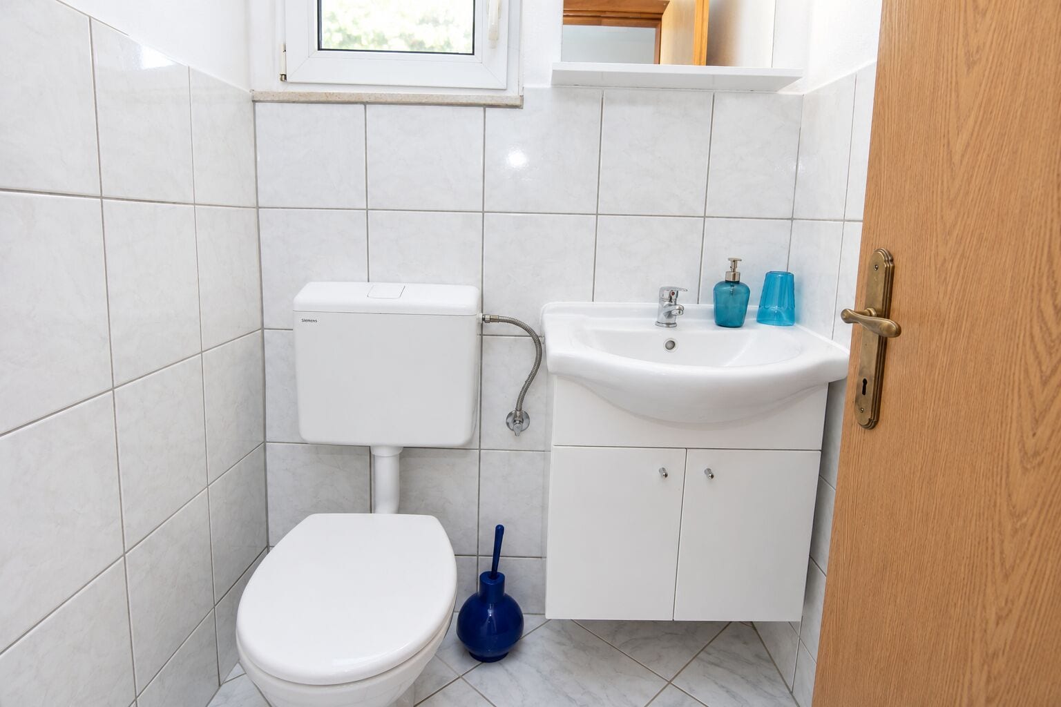 A small bathroom with a toilet, sink, and blue plunger.