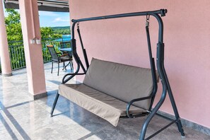 A patio with a swing chair, a table with chairs, and a view of greenery. - Apartment Kaleta (Rogoznica)