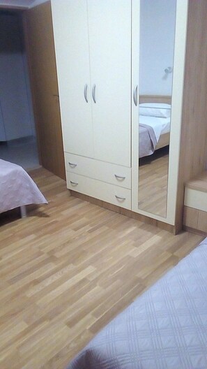 A bedroom with a wooden floor, a bed, a wardrobe with two doors, and a mirror. - Apartment Kaleta (Rogoznica)