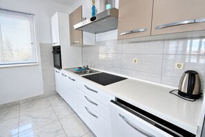 A modern kitchen with white cabinets, a black countertop, and a stainless steel kettle. - Apartment Kaleta (Rogoznica)