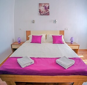 A neatly made bed with a wooden headboard, two bedside tables with lamps, and a wall-mounted picture. - Apartment Kaleta (Rogoznica)