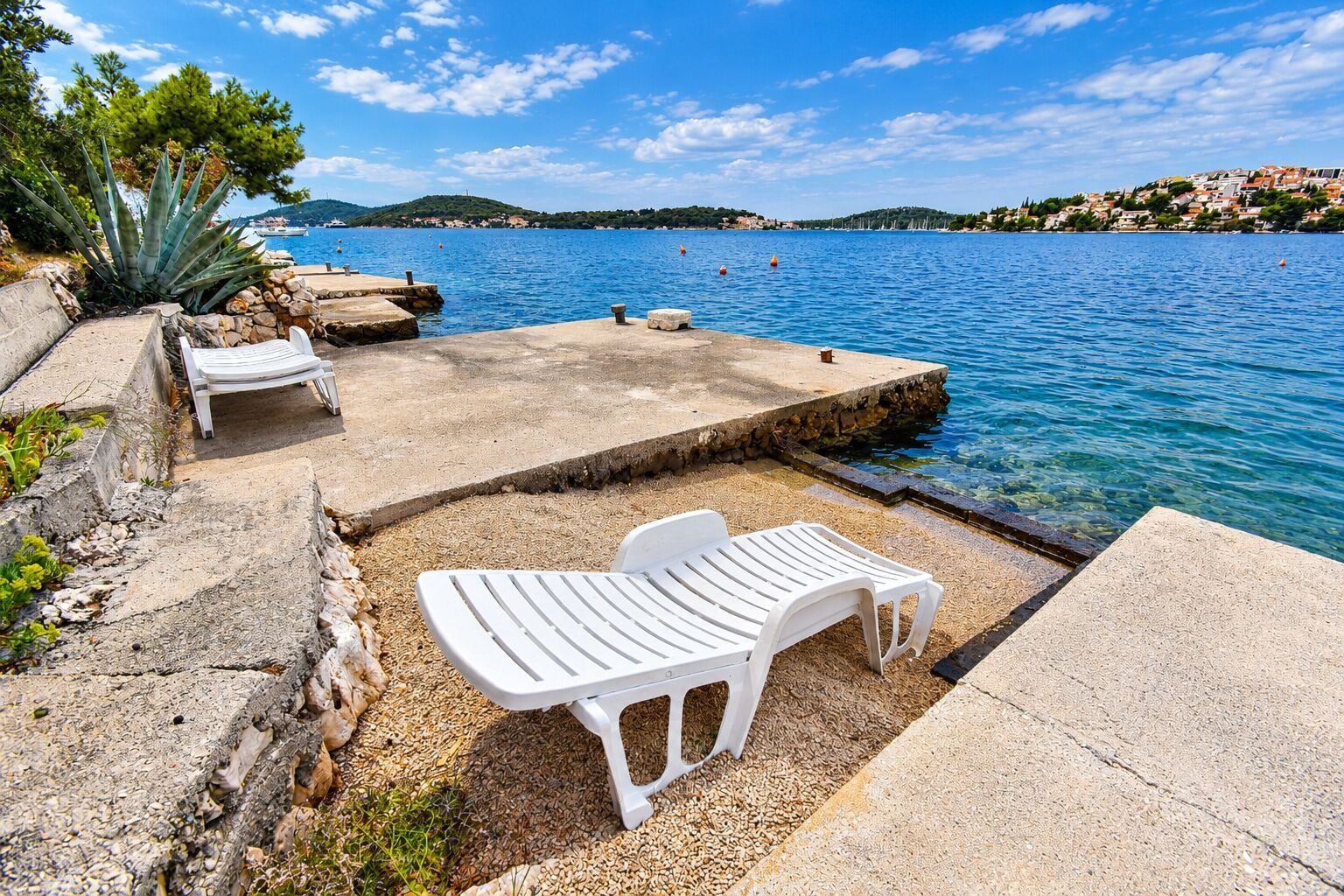 Un patio frente al mar con sillas y una mesa de plástico blanco, con vista a un mar azul transparente.
