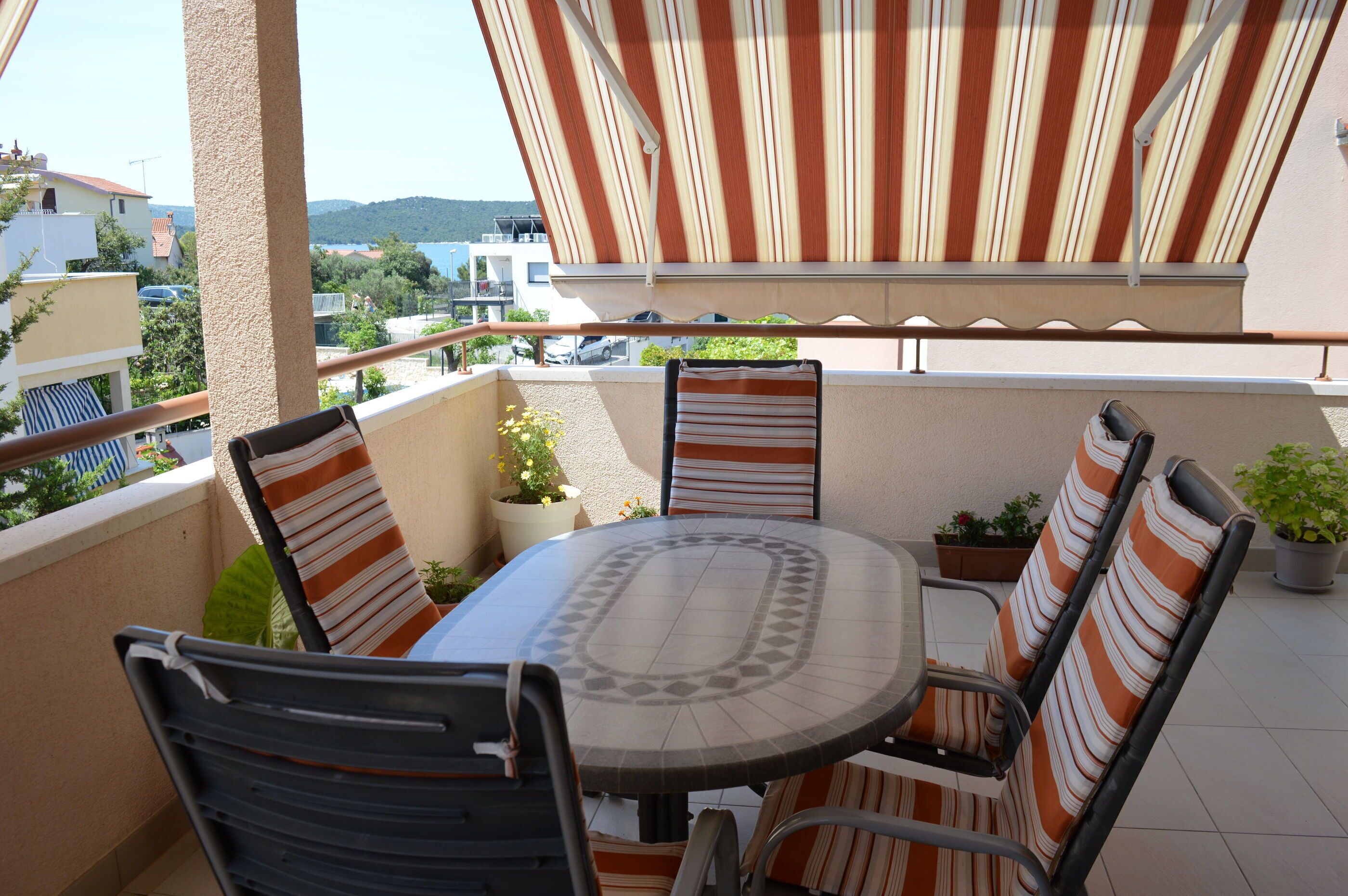 A balcony with a striped awning, a round table, and four striped chairs.