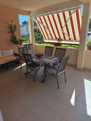 Ein überdachter Patio-Bereich mit Tisch, Stühlen und einer Couch, mit Blick auf grüne Vegetation.