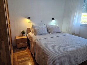 Ein Schlafzimmer mit einem Bett, Nachttischen, einer Stehlampe, einem Topf mit Pflanze und einem Fenster mit Vorhängen.