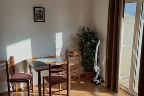 Ein Zimmer mit einem Holztisch, vier Stühlen, einer Topfpflanze und einer Schiebeglastür.