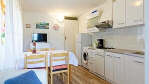A compact kitchen with a washing machine, a dining area with a table and chairs, and a sofa with a blue cushion. - Apartments Durdica (Umag)