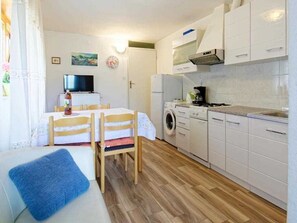 A compact kitchen with a washing machine, a dining area with a table and chairs, and a sofa with a blue cushion. - Apartments Durdica (Umag)