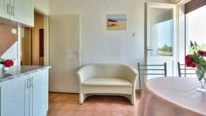 A room with a white sofa, a dining table with a vase of flowers, a cabinet with drawers, and a painting on the wall. - Apartments Durdica (Umag)