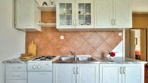 A kitchen with a gas stove, sink, and marble countertops. There are cabinets with glass doors above the sink. - Apartments Durdica (Umag)