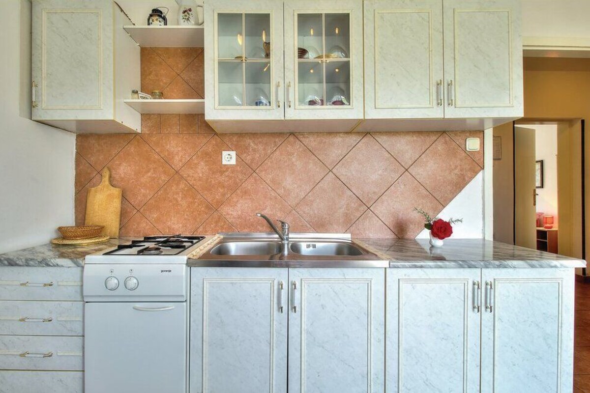 A kitchen with a gas stove, sink, and marble countertops. There are cabinets with glass doors above the sink.