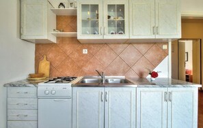 A kitchen with a gas stove, sink, and marble countertops. There are cabinets with glass doors above the sink. - Apartments Durdica (Umag)