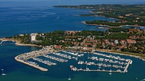 An aerial view of a coastal town with a marina filled with boats, surrounded by residential buildings and greenery. - Apartments Durdica (Umag)