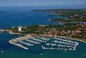 An aerial view of a coastal town with a marina filled with boats, surrounded by residential buildings and greenery. - Apartments Durdica (Umag)