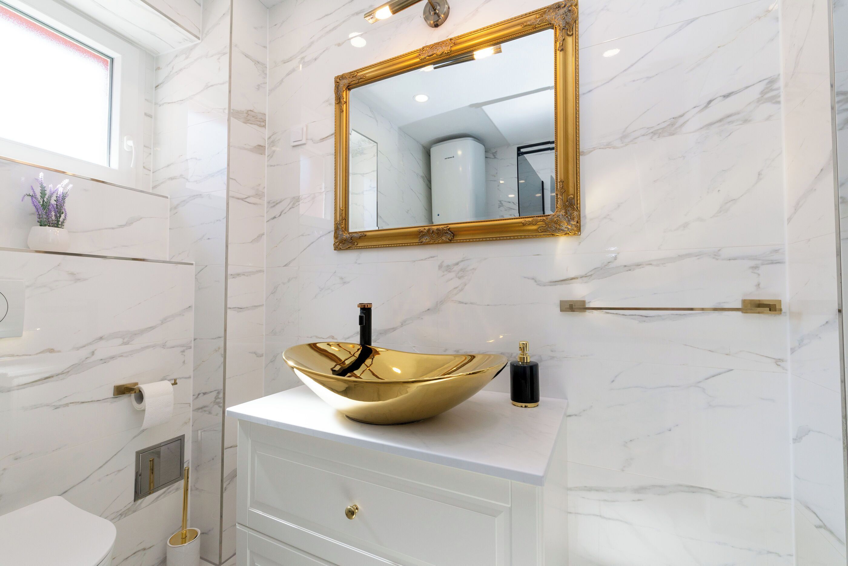 A bathroom with a white marble sink, gold-framed mirror, and a toilet.