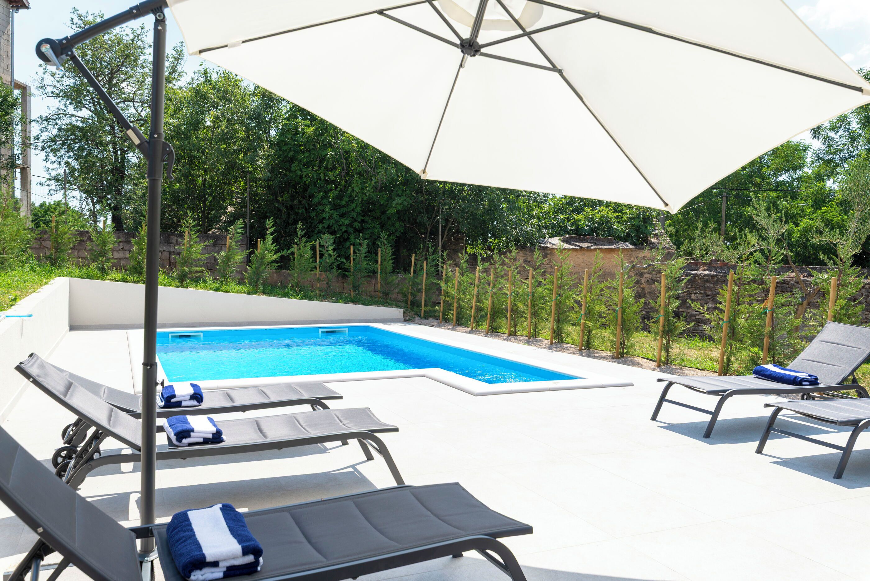 A swimming pool with lounge chairs and a large umbrella.